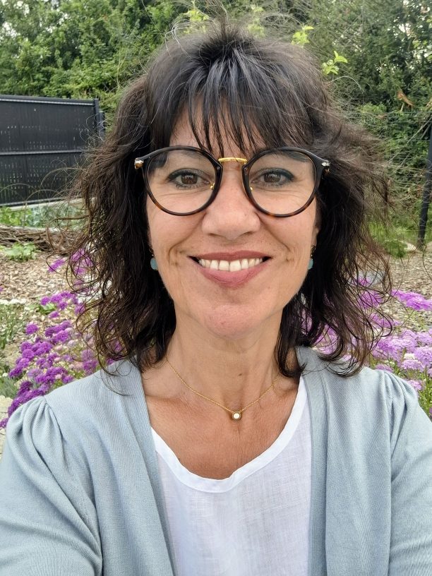 Carine Grondin, naturopathe, souriante devant un massif de fleurs mauves