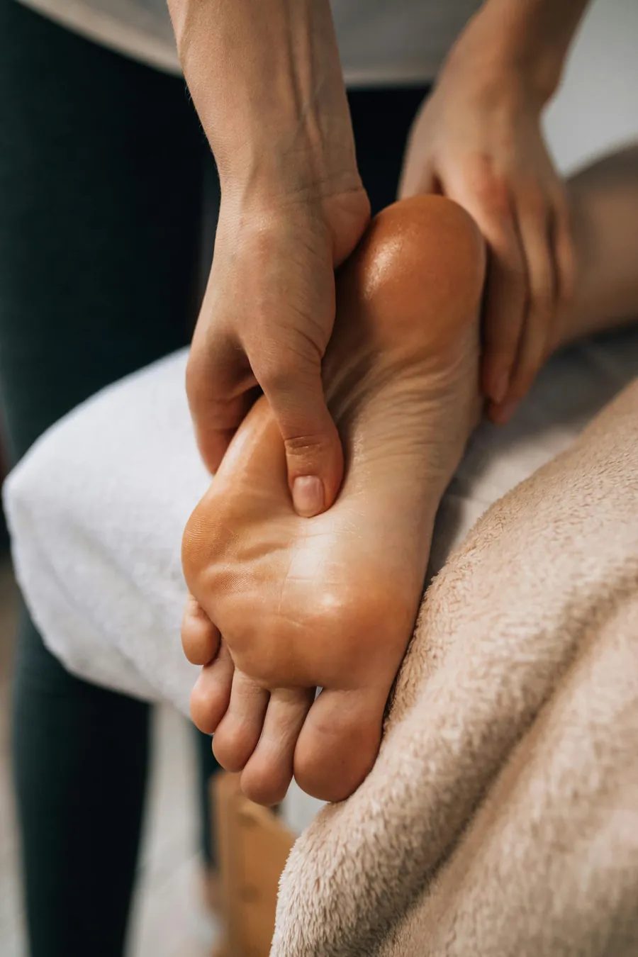 Mains de la praticienne exerçant des pressions sur la plante d'un pied posé sur une serviette